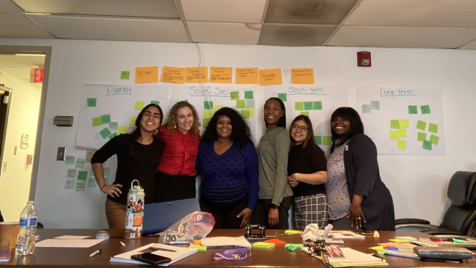 A group of CSAJ staff members and DASH advocates, representing a diverse mix of ethnicities, smiling at camera and standing close together in front of a wall covered in sticky notes.