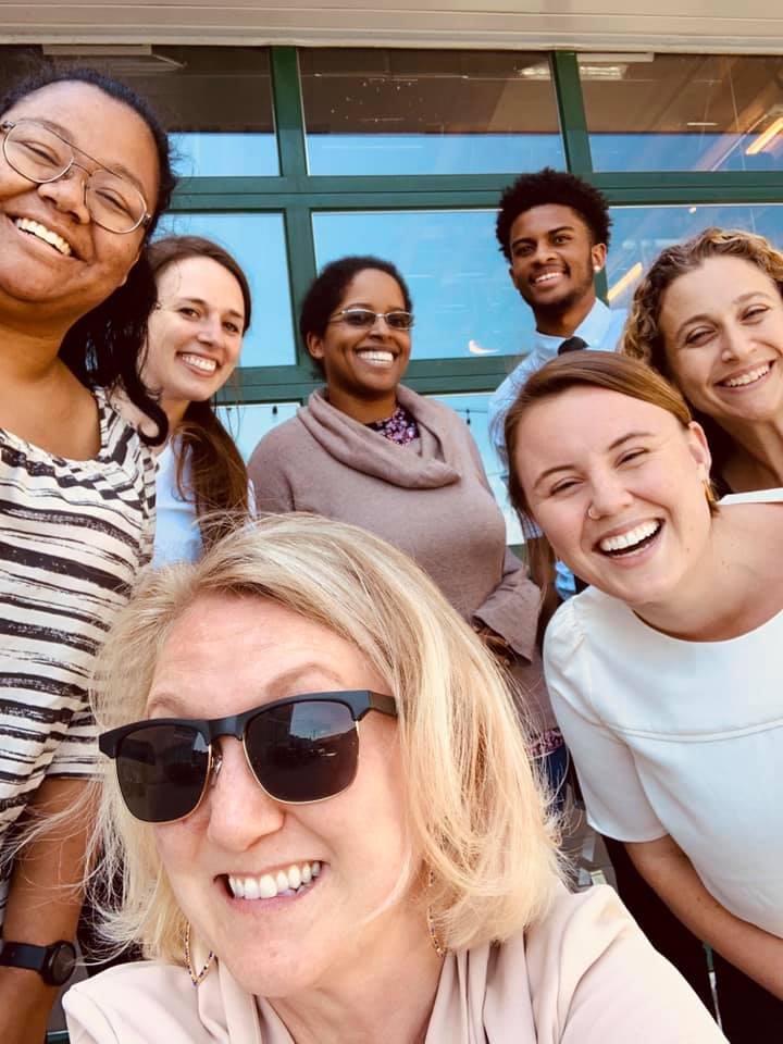 CSAJ staff member Sara and 6 summer interns of diverse genders and ethnicities take a selfie together outside, with big smiles on their faces.